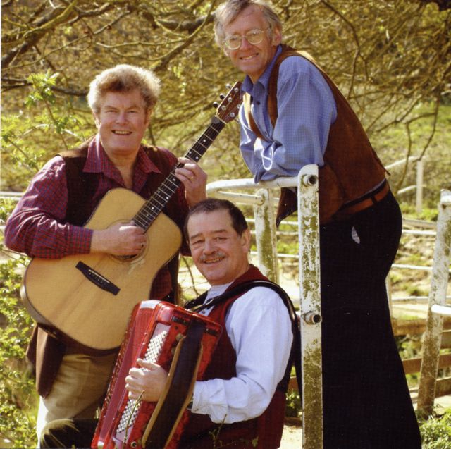 The Yetties outdoors by a white railing, one with a guitar and one with an accordion