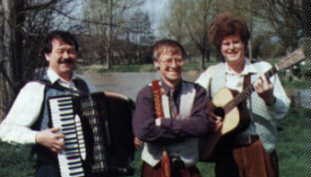 Three musicians by a river, with an accordion and a guitar
