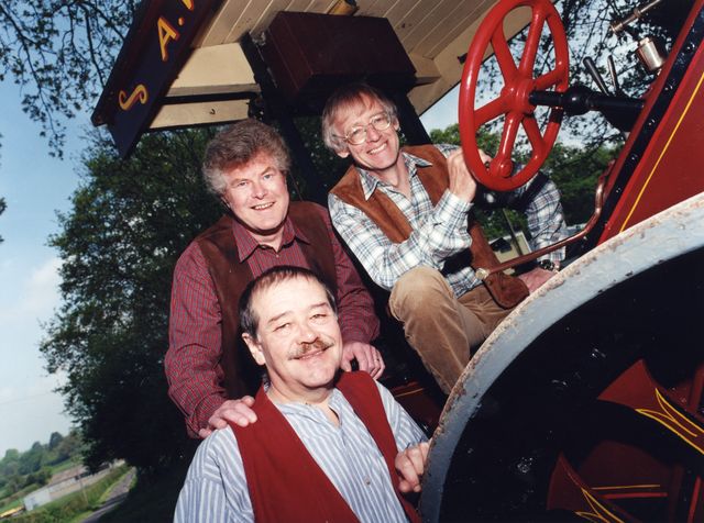 The three on the footplate of a traction engine with a red steering wheel